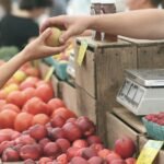 A customer exchanges an apple with a vendor at a vibrant farmers market.